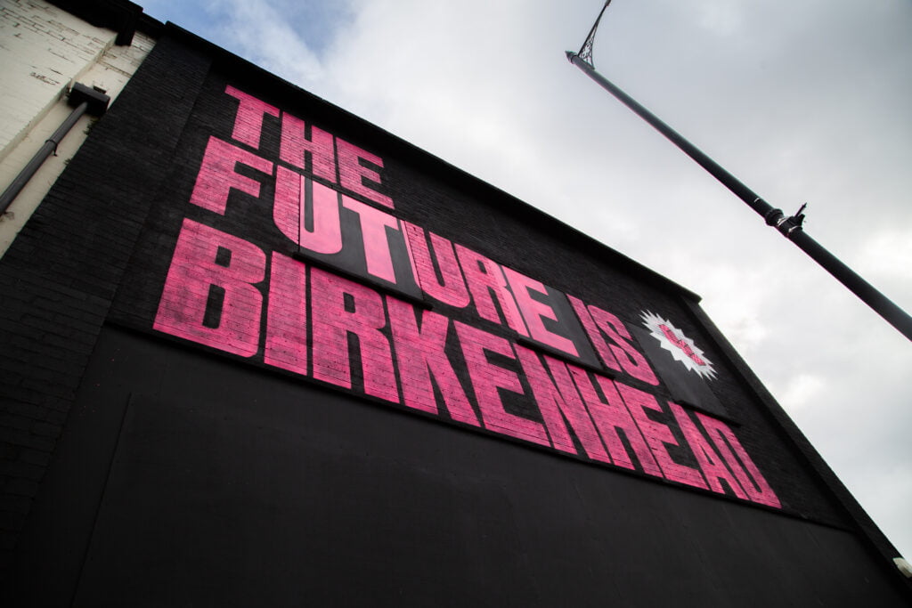 Pink writing the future is birkenhead on black background, on an outside wall