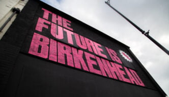 Pink writing the future is birkenhead on black background, on an outside wall