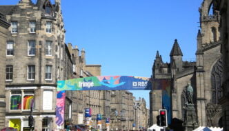 View of Edinburgh street during the festival, with large colourful banner saying 'Fringe' and crowd of people below it