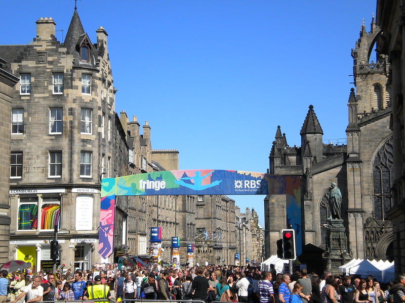 View of Edinburgh street during the festival, with large colourful banner saying 'Fringe' and crowd of people below it