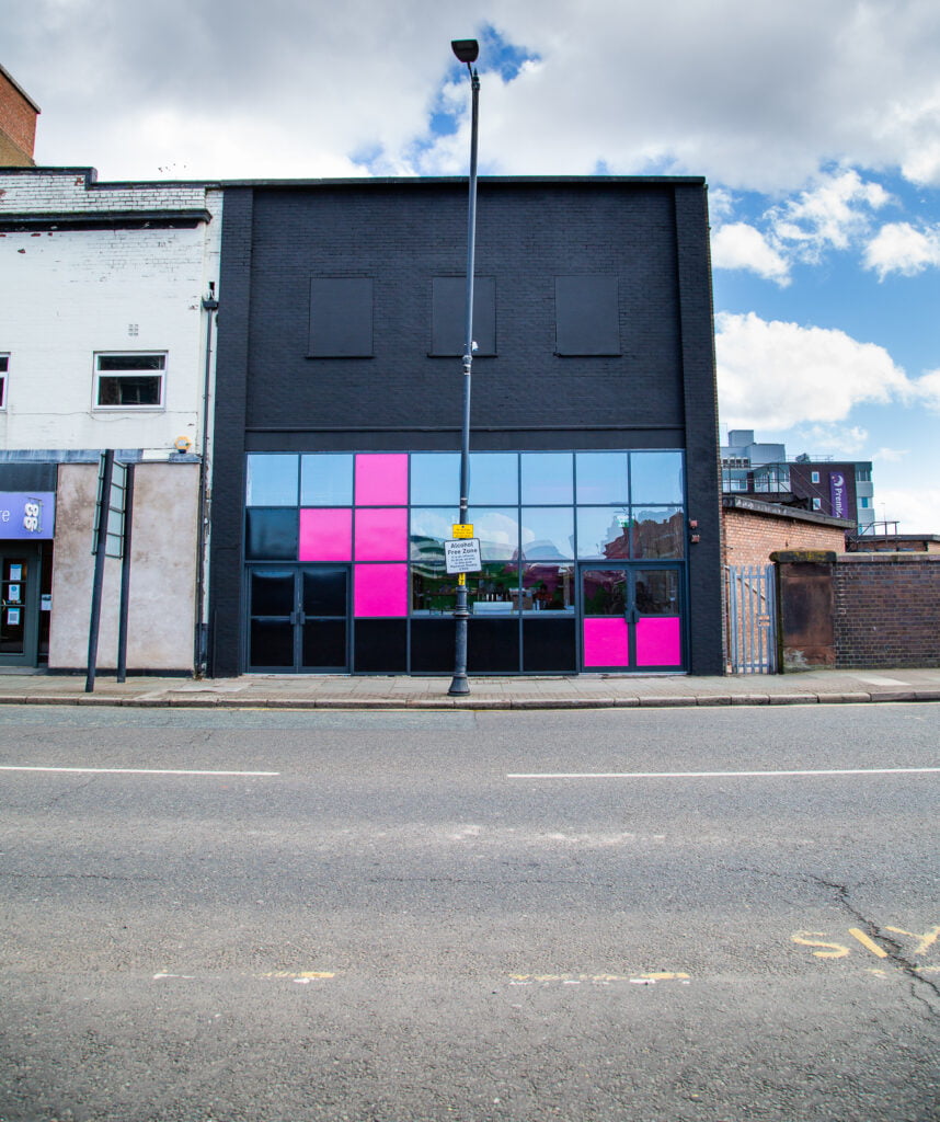 Black building seen from acros the street, with black and pink window panes on the bottom half