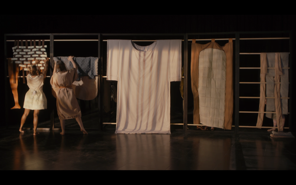 Film still from video shows performers interacting with textile pieces hung on a metal frame