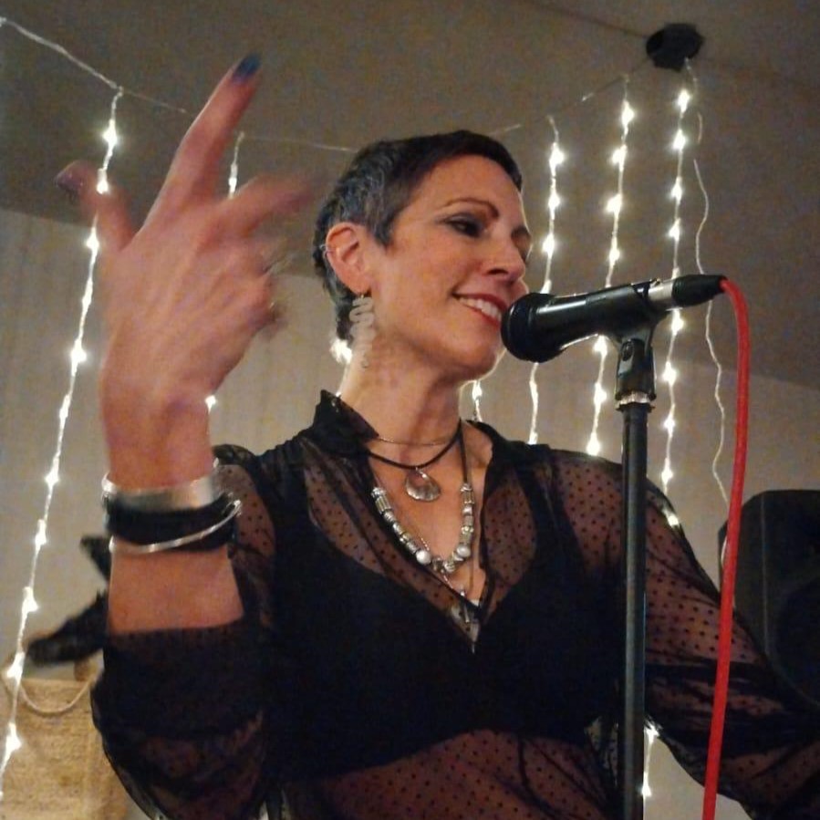 Image of Sarah stood at a microphone performing poetry.
