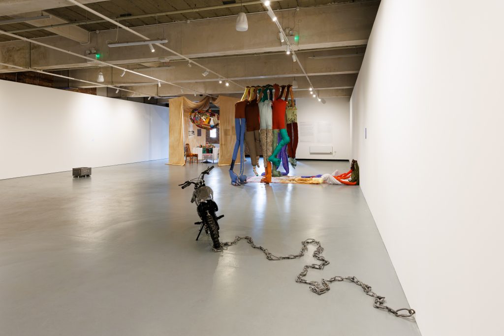 Image of the exhibition featuring the Preston's pit bike, Mirza's fabric figures and in the distance Saddiqui's installation.