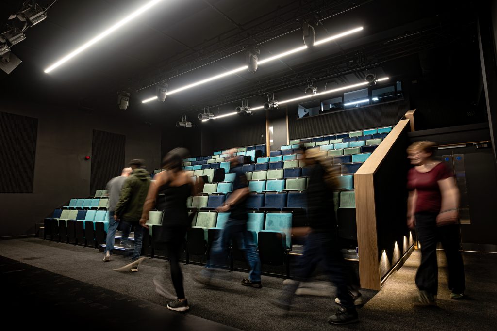 Image of the new theatre seats, with people walking in to fill them.