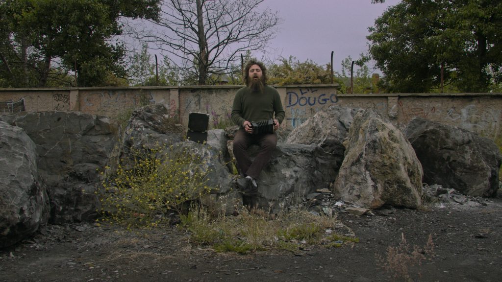 Image of man sat on a rock playing folk music. 