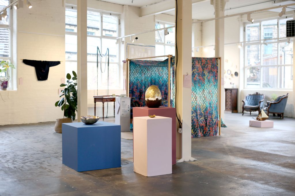 Wide shot of the gallery with objects displayed on boxes of different heights and colours.