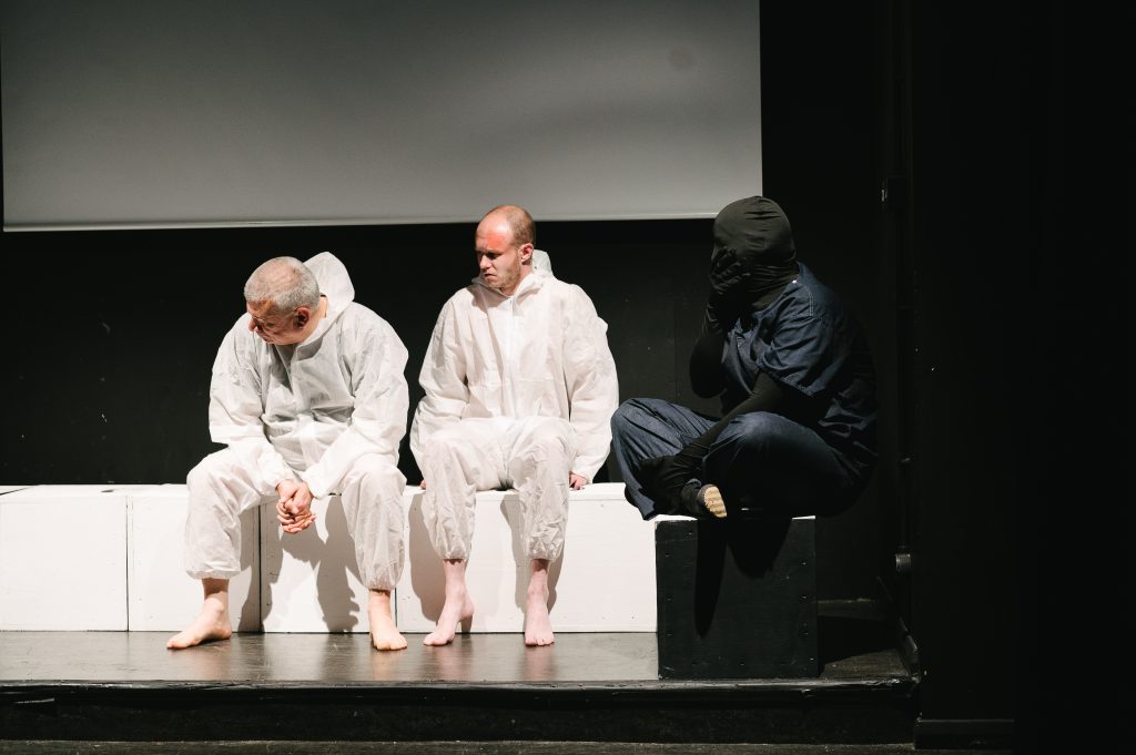 Winston and Parsons sit on white boxes underneath a projector looking worried. 