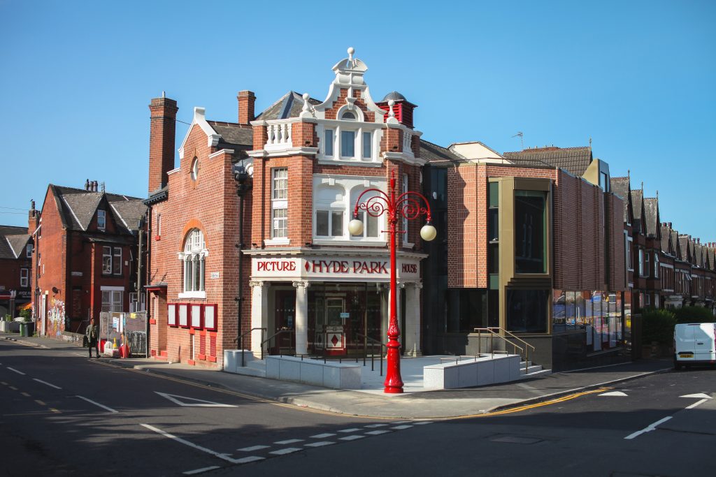 Exterior of Hyde Park Picture House, a red-brick cinema on a street corner with white pillars at the entrance and a decorative red lamppost in front.