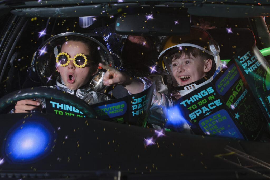 Lenny and Mullet sit in the front seats of a car, wearing astronaut suits and reading magazines which say 'Thing To Do in Space.'