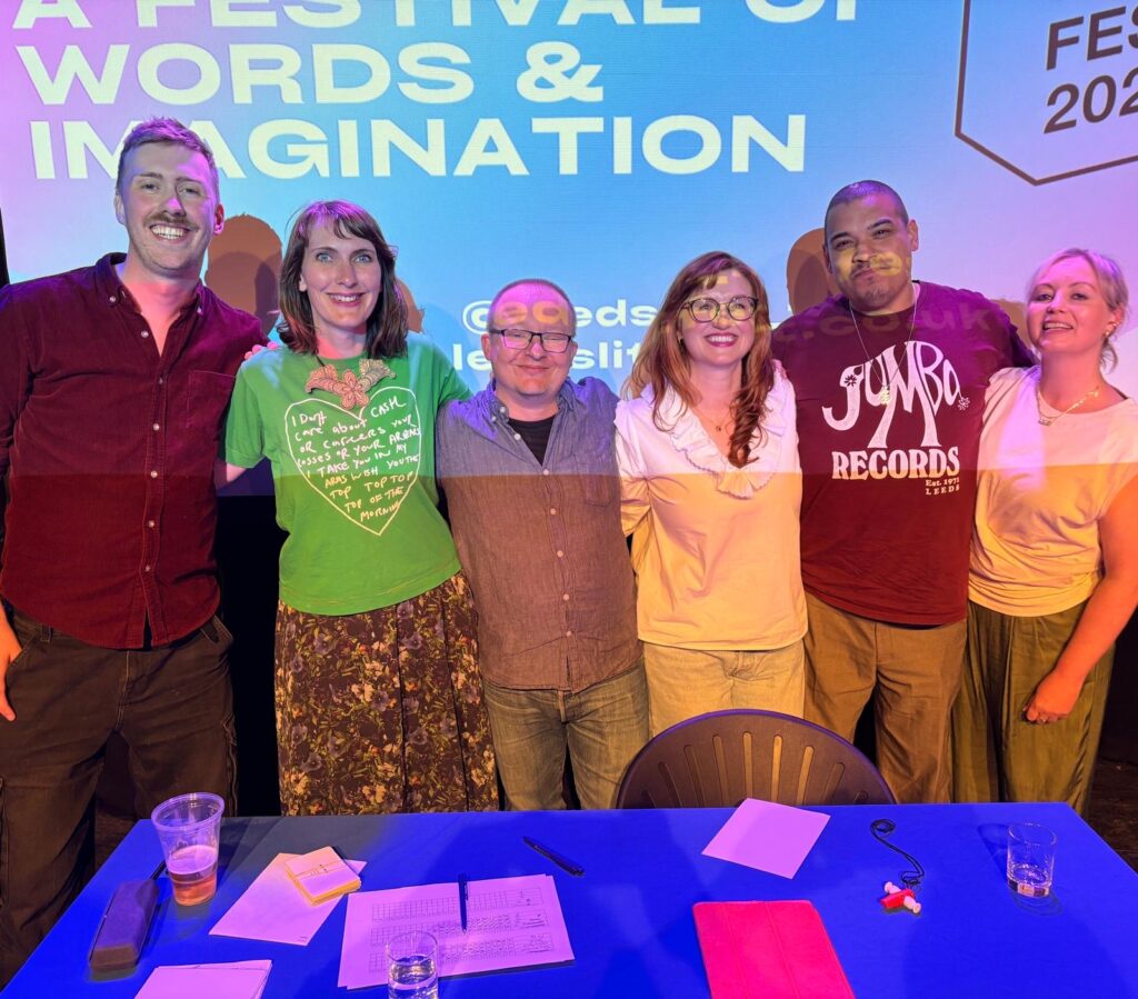 Six people stand in front of a table covered by a blue table cloth and papers.