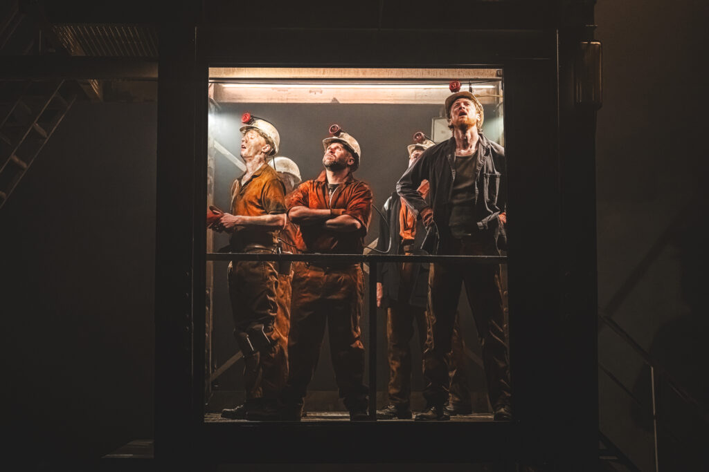 Miners in a cage lift during Brassed Off at Leeds Playhouse, depicting the claustrophobic conditions of life underground.