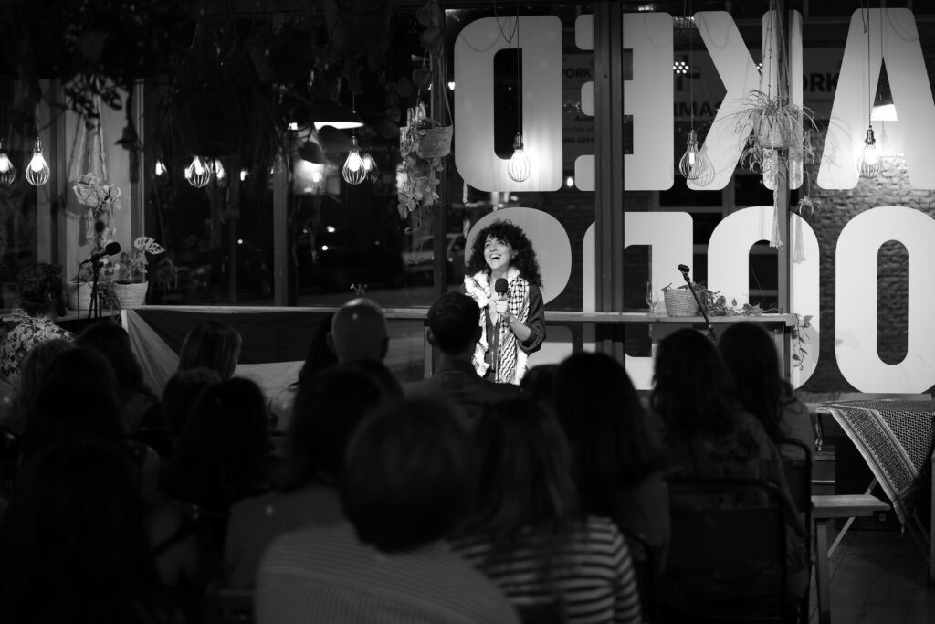 Black and white picture of Farah standing in front of a seated crowd with a microphone in hand laughing.