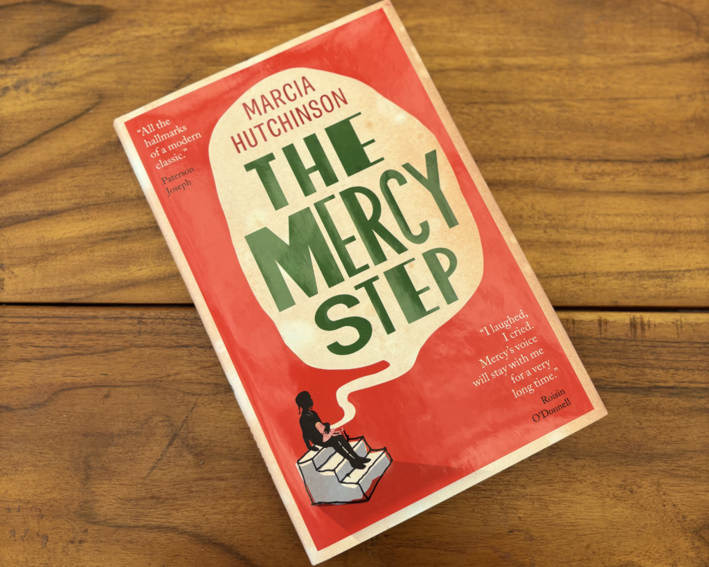 'The Mercy Step' book lies face up on a wooden table.