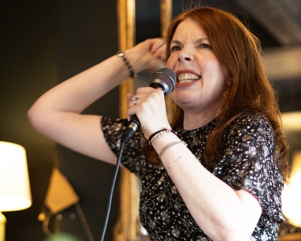 Anne-Marie Draycott grimaces into the microphone, waving her arm in the air, at the That’s What She Said poetry event at The Cardigan Arms in Leeds.